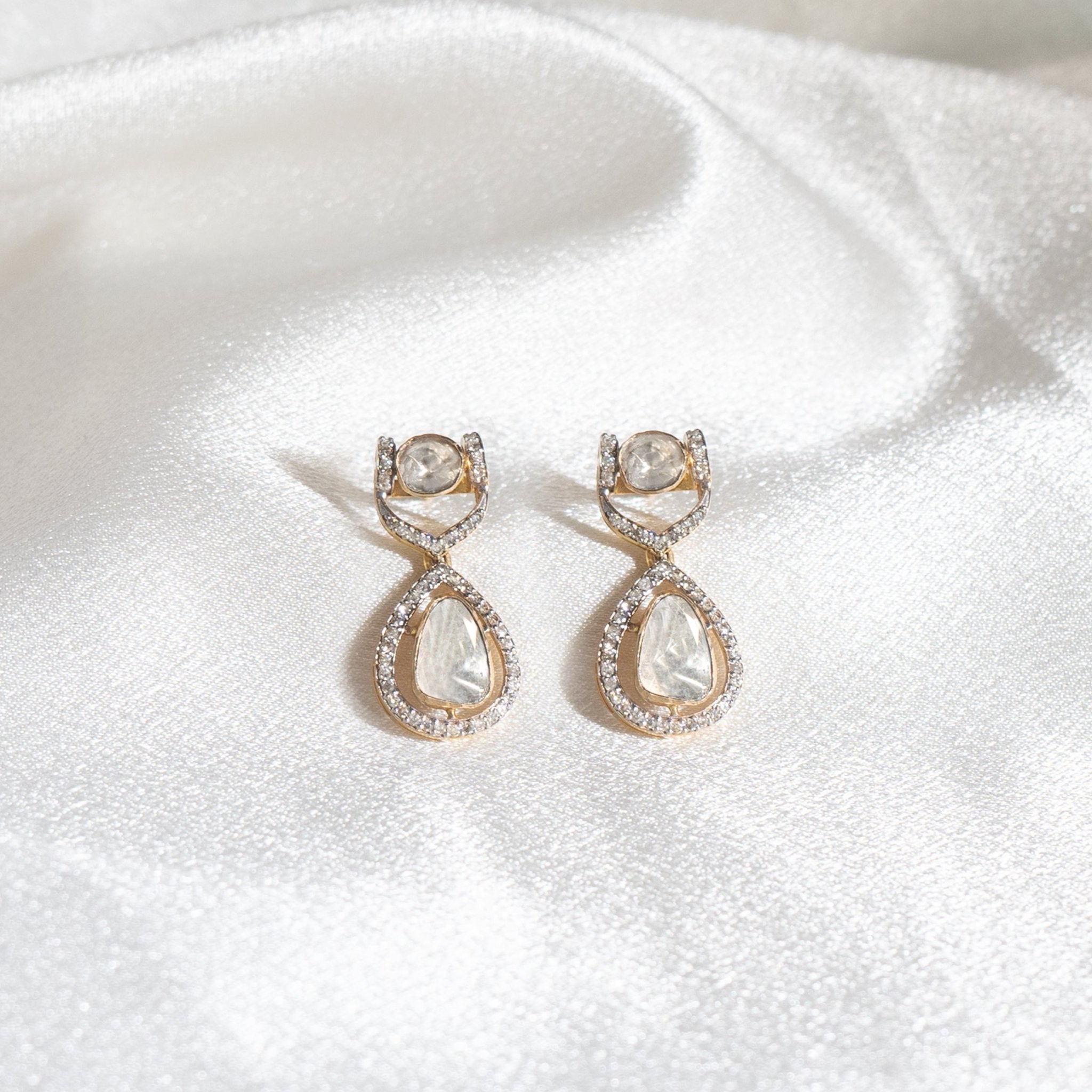 Subtle luxury polki earrings in miniature drop shape resting on minimal ivory silk.