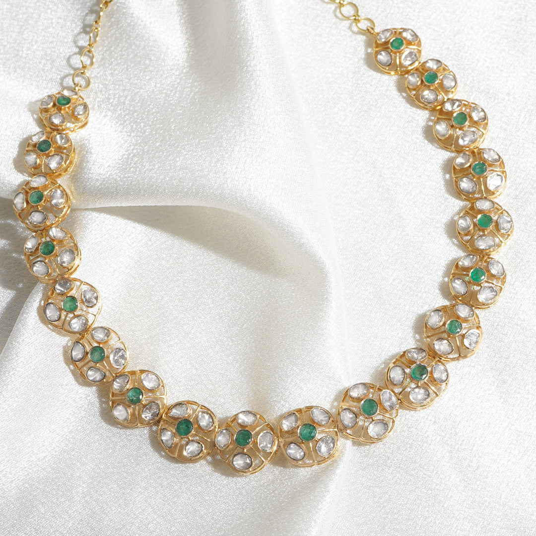 18k gold necklace with intricate floral polki design, emerald center, and sumptuous gold chain.